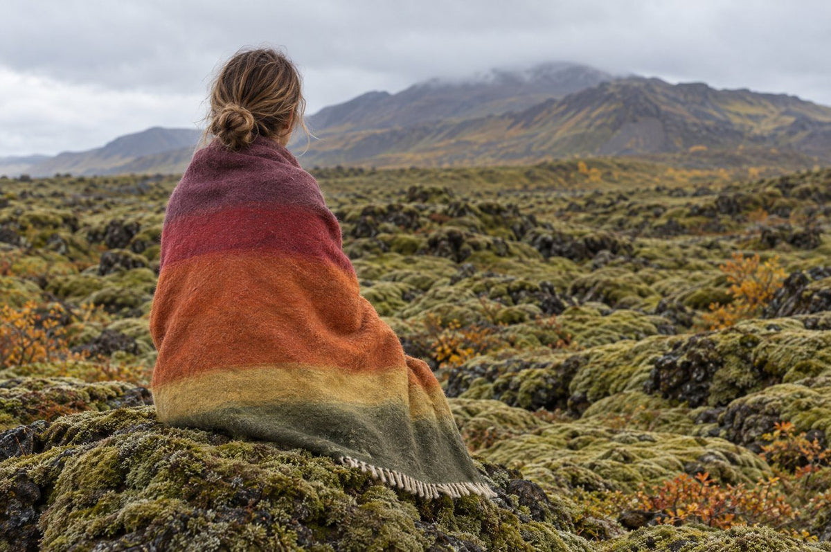 Woman wrapped in the Flói Earth wool blanket on a moss-covered lava field