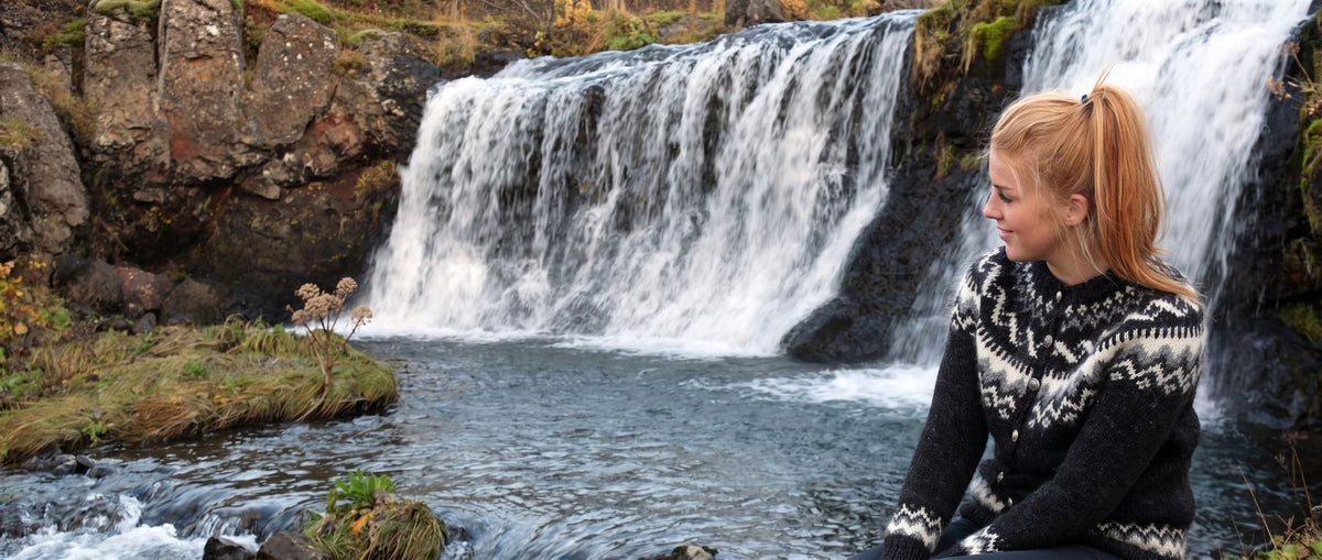 Woman in a dark Icelandic wool sweater by a waterfall