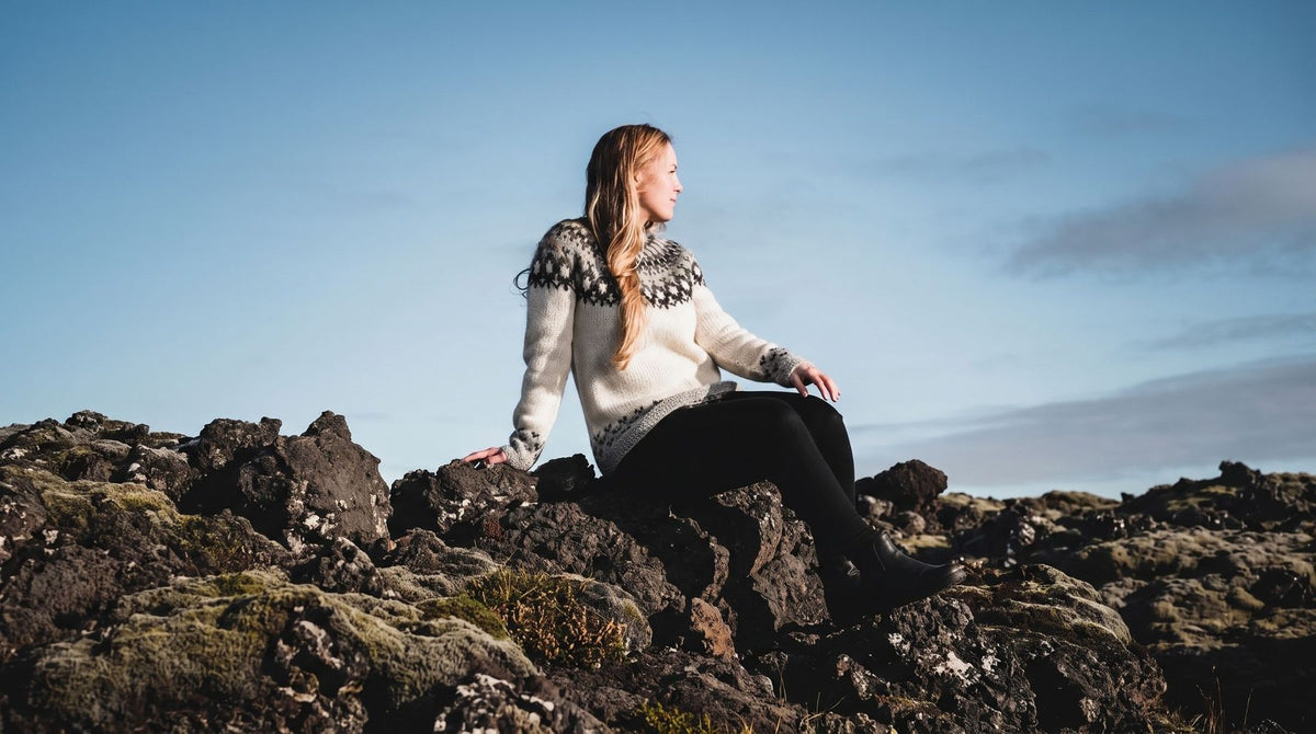 Woman in a white Icelandic wool sweater sitting on lava rocks